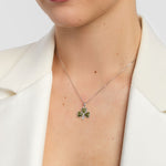 Person wearing a silver necklace with a clover-shaped pendant on a white background