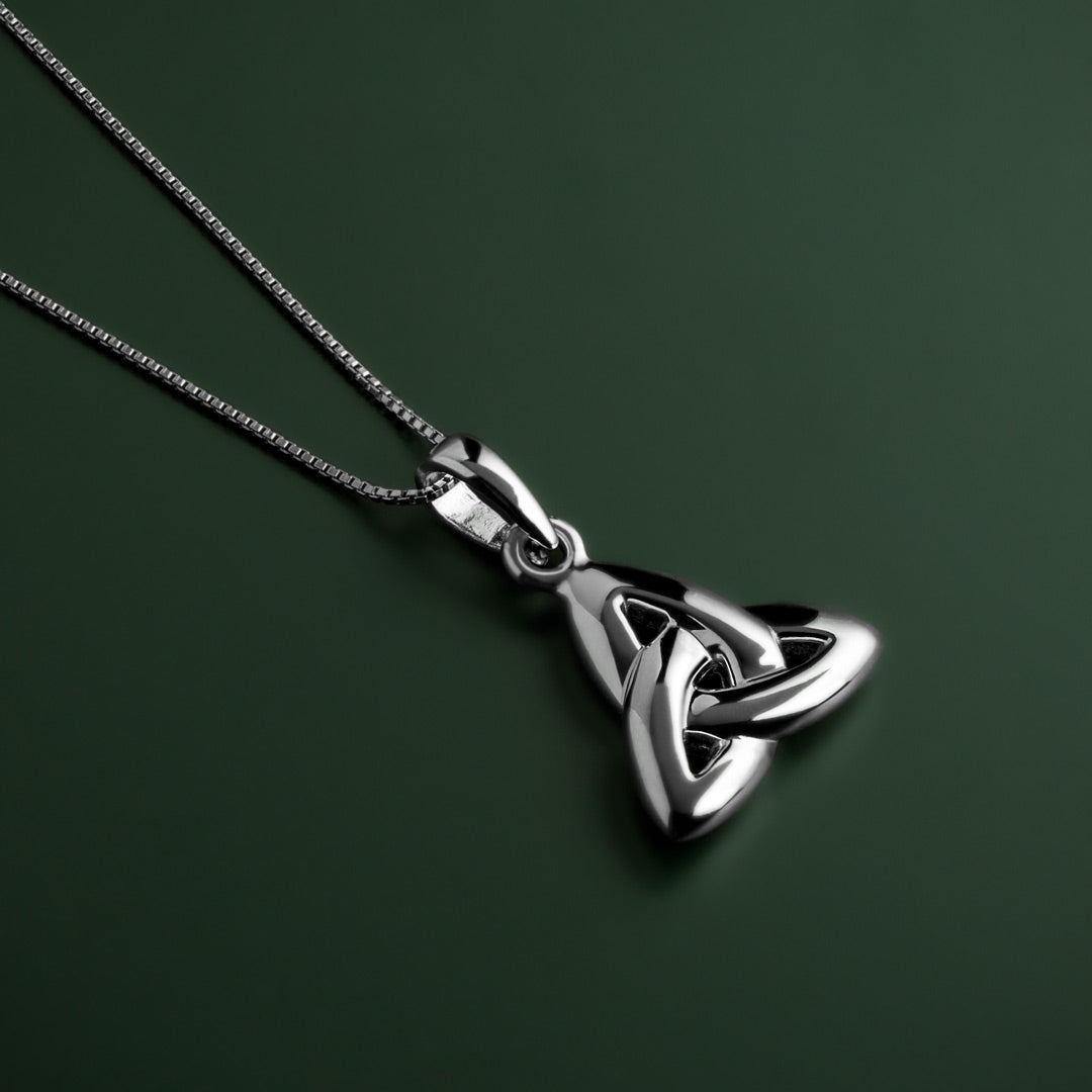 lifestyle image of double-sided trinity knot pendant on green background