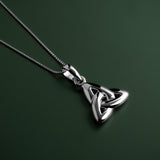 lifestyle image of double-sided trinity knot pendant on green background