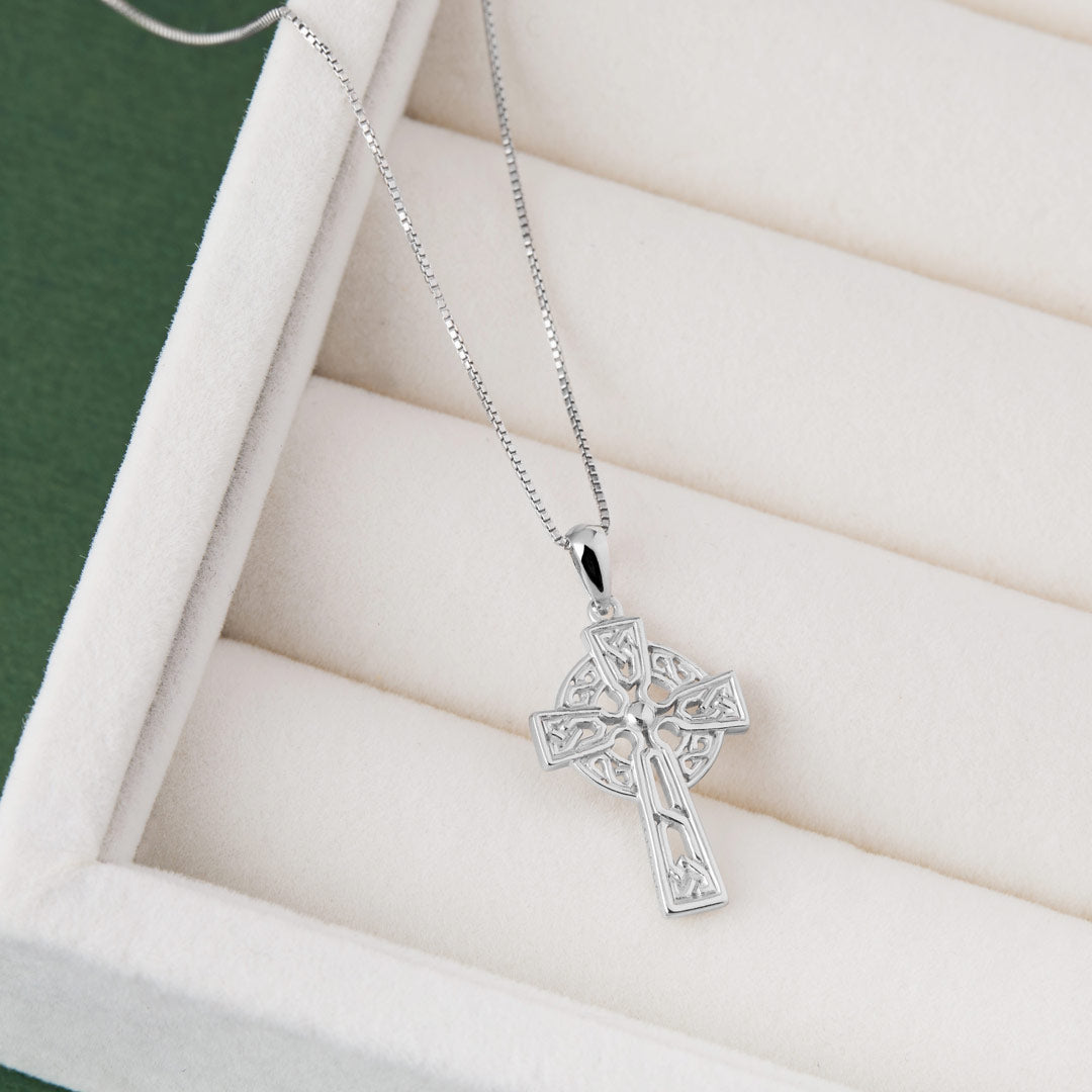 Silver cross pendant necklace on a white cushioned surface