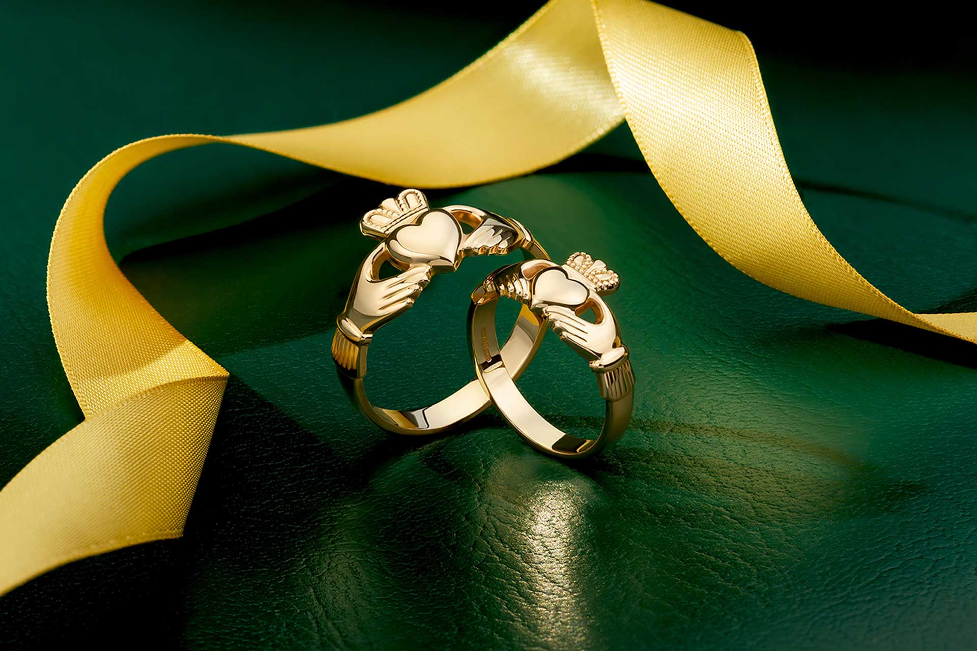 lifestyle image of a set of two gold claddagh rings and yellow ribbon at the background