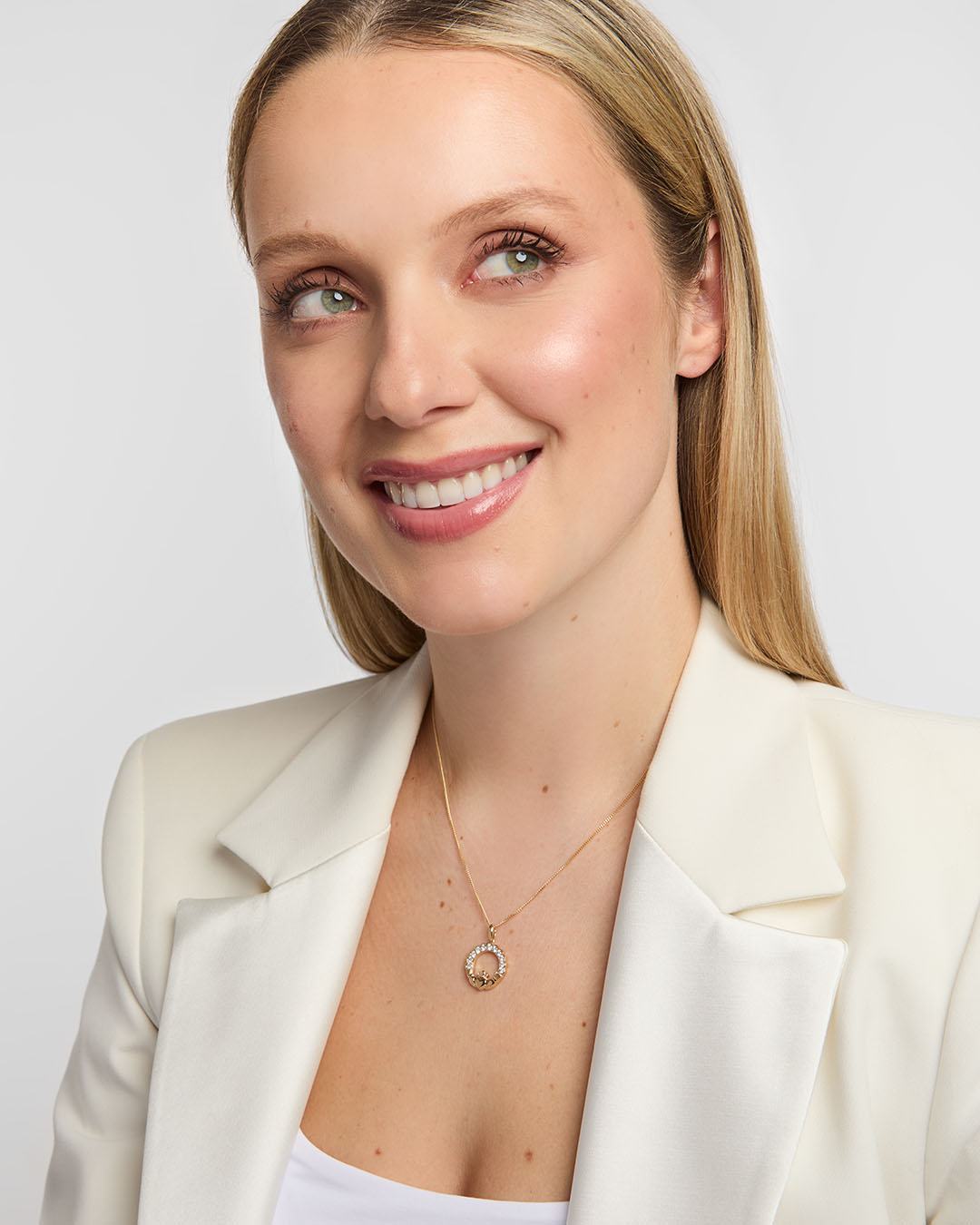 Female model wearing a radiant 14K gold Claddagh pendant with a shimmering diamond halo
