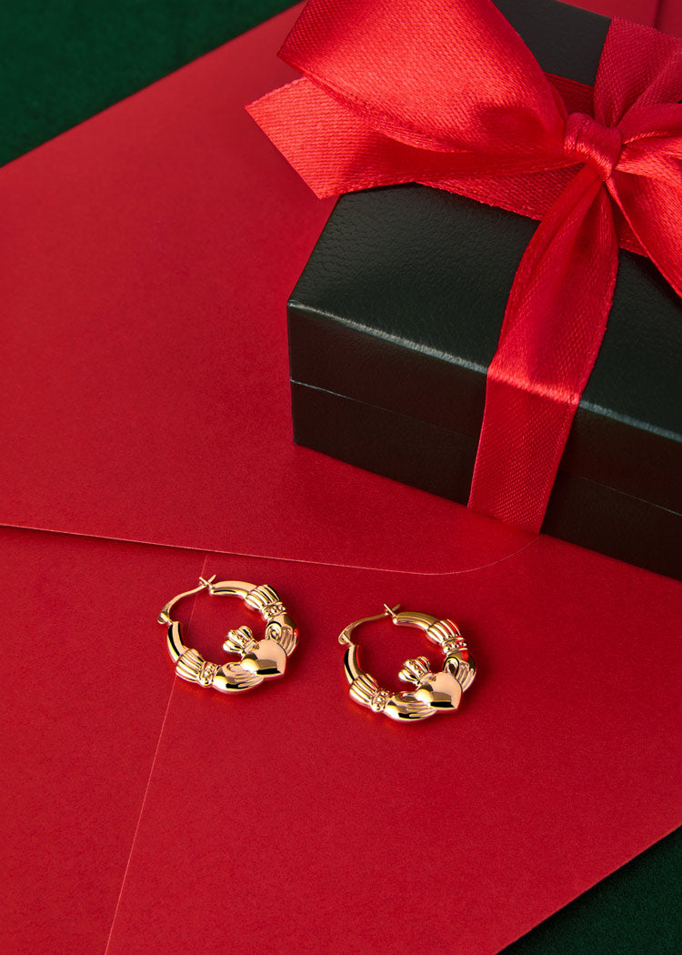 festive-styled  image of gold hoop claddagh earrings  from Solvar on red background