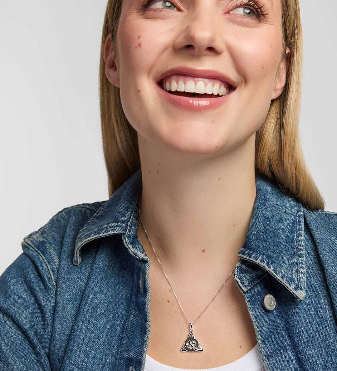 model wearing a polished silver Trinity Knot  pendant entwined around a circular green marble inlay, combining flowing Celtic lines with a clean, openwork finish.