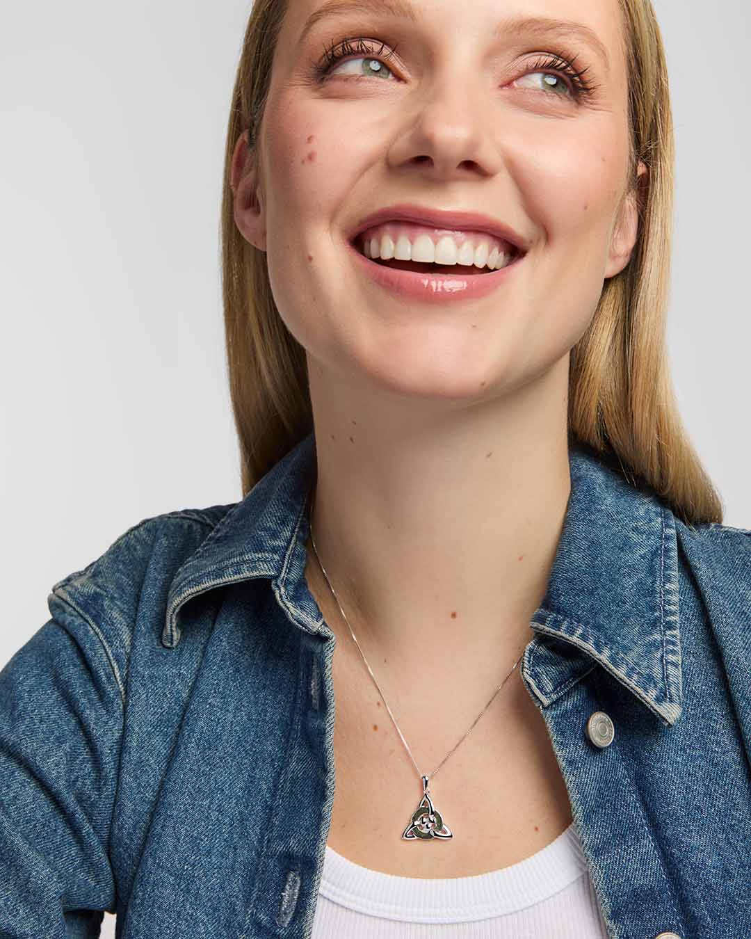 model wearing a polished silver Trinity Knot  pendant entwined around a circular green marble inlay, combining flowing Celtic lines with a clean, openwork finish.