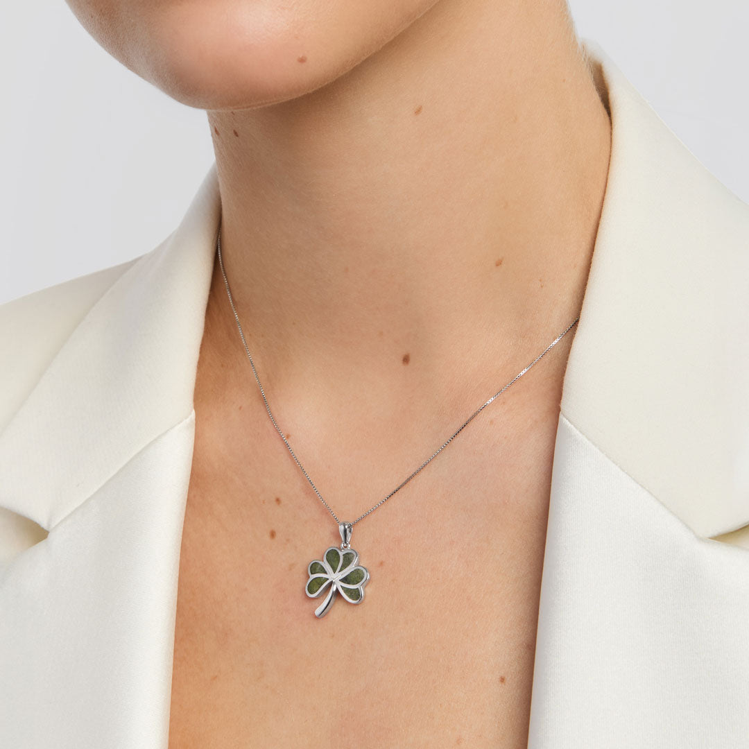 Person wearing a silver necklace with a shamrock pendant on a white background