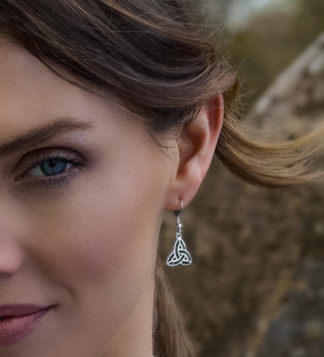 Close-up of a female model wearing a green marble Trinity Knot earring with a blurred natural background