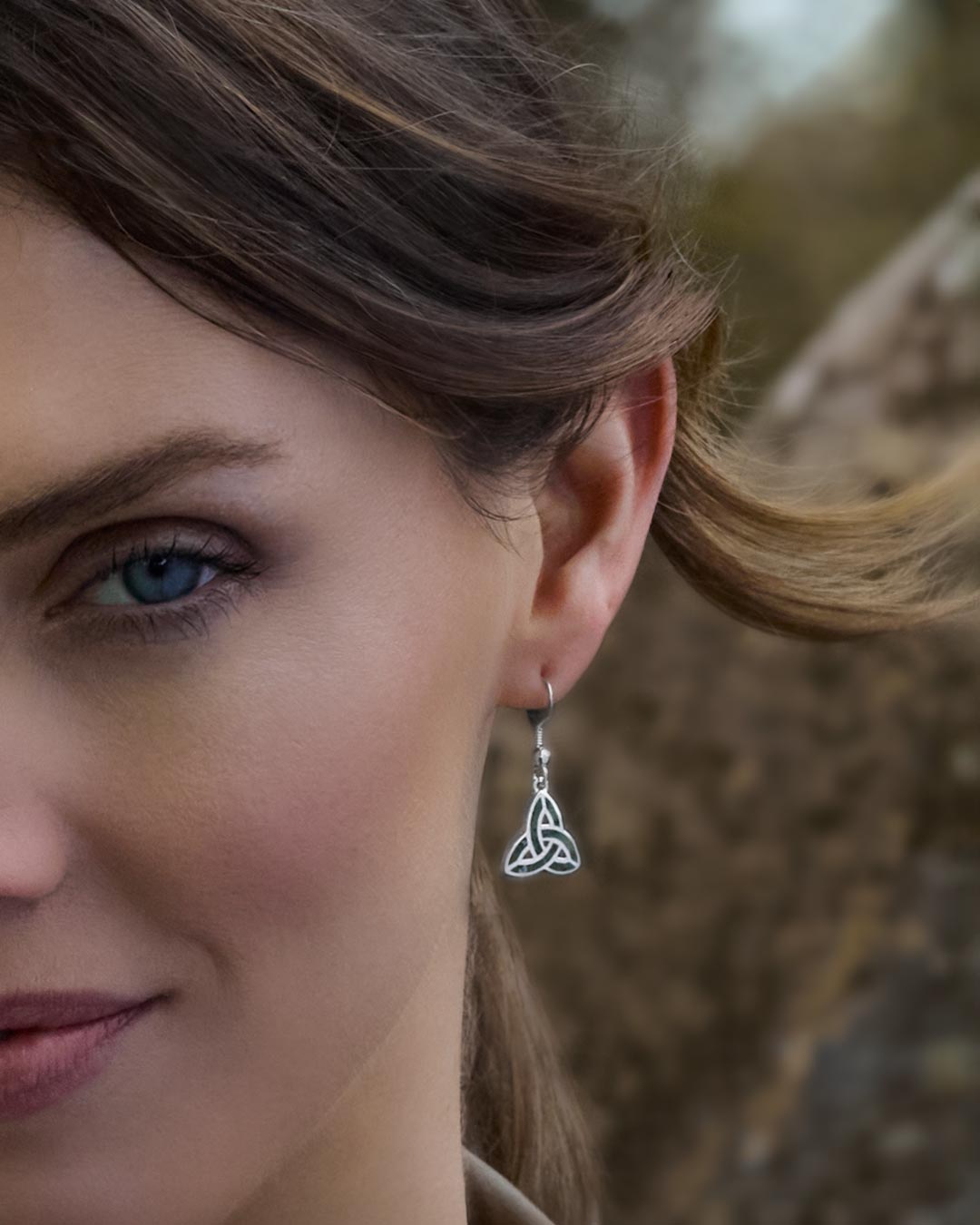 Close-up of a female model wearing a green marble Trinity Knot earring with a blurred natural background