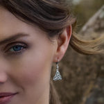 Close-up of a female model wearing a green marble Trinity Knot earring with a blurred natural background