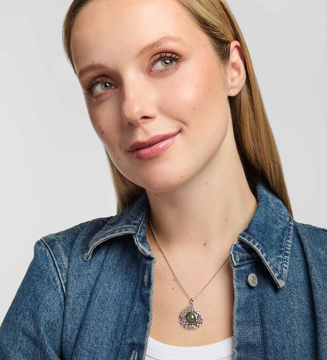 A close-up of a woman showcasing a Celtic-style pendant built around a large round green marble, with the surrounding silver-toned design combining interlacing knotwork and small shamrock motifs.