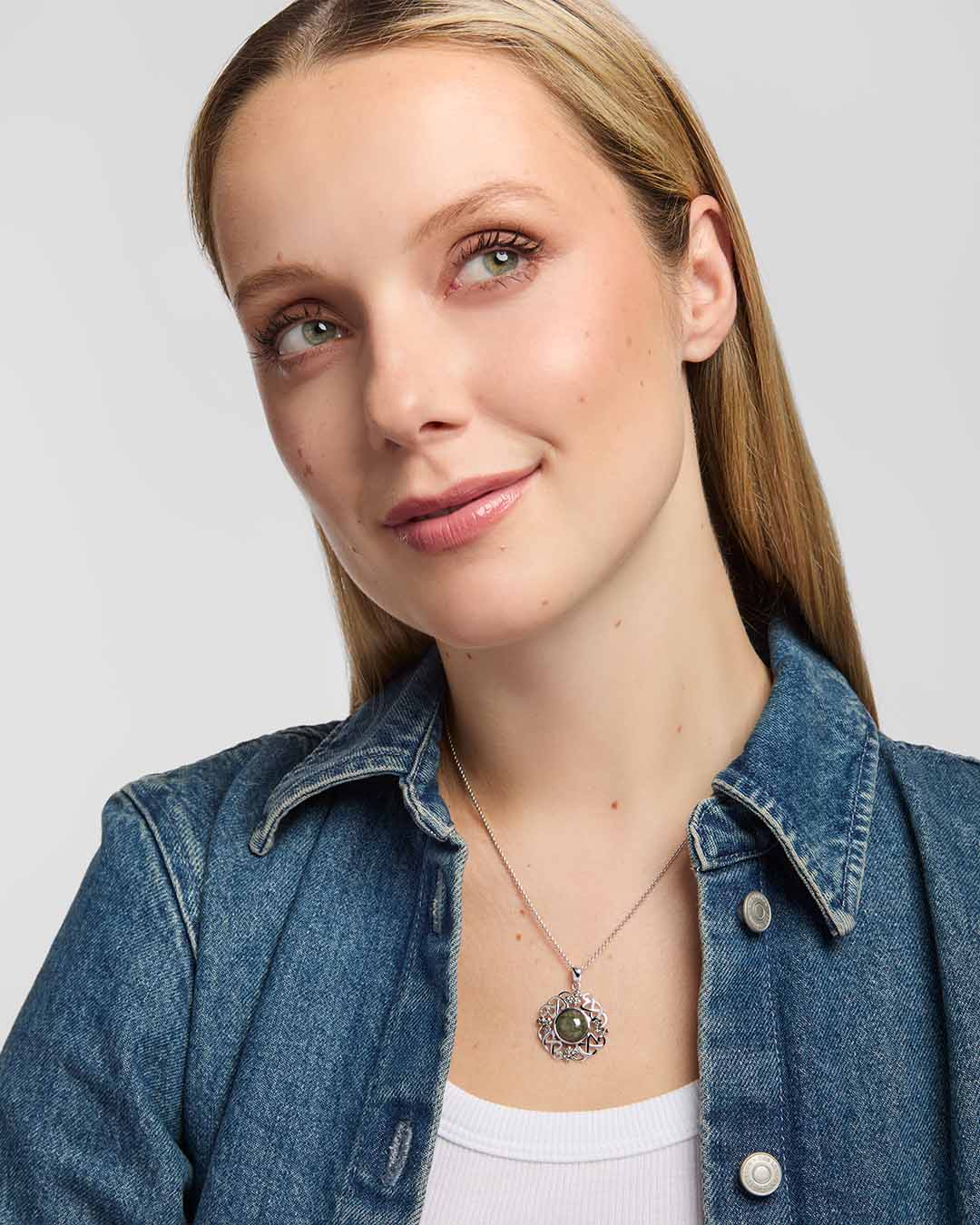A close-up of a woman showcasing a Celtic-style pendant built around a large round green marble, with the surrounding silver-toned design combining interlacing knotwork and small shamrock motifs.