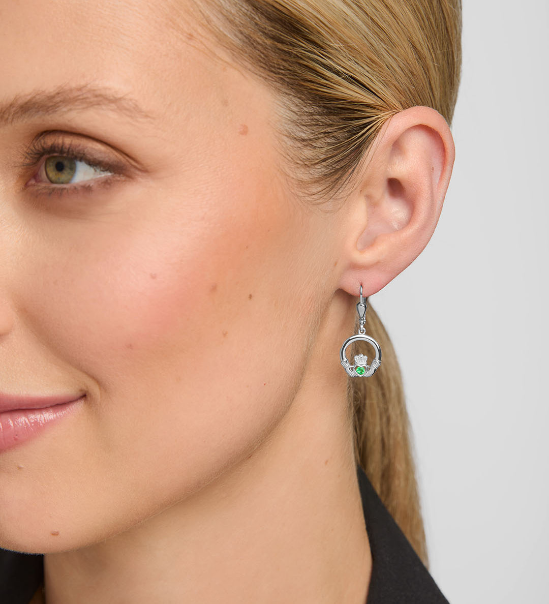 close-up image of a model wearing green crystal claddagh drop earrings in silver