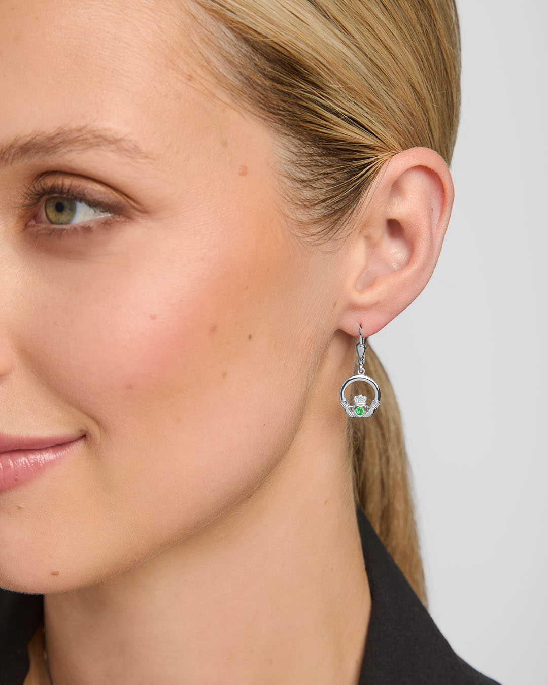 close-up image of a model wearing green crystal claddagh drop earrings in silver