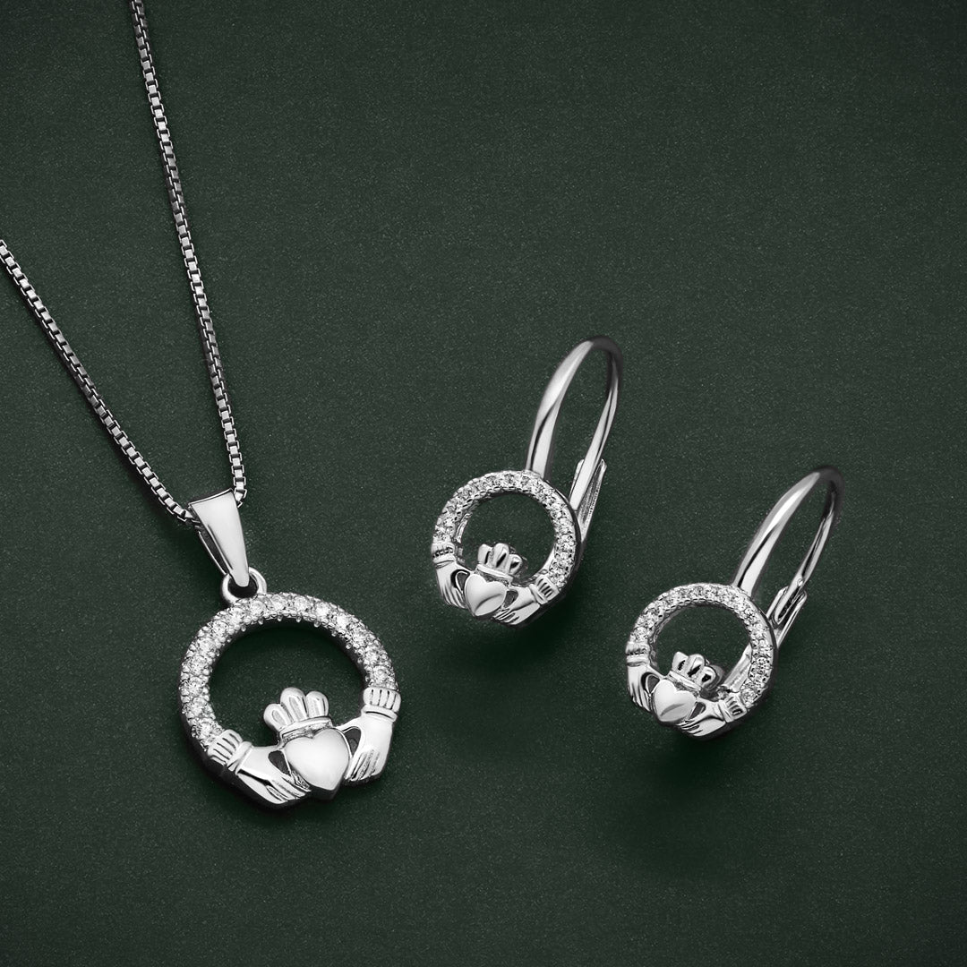 a lifestyle image featuring matching cubic zirconia claddagh pendant and earrings on a green background