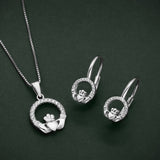 a lifestyle image featuring matching cubic zirconia claddagh pendant and earrings on a green background