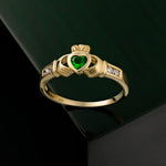 lifestyle image of yellow gold Emerald & Cz Claddagh Ring on dark green backgrouind