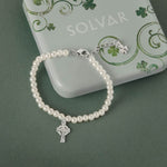 Celtic pearl bracelet with a silver Celtic cross charm on a green background