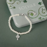 Celtic pearl bracelet with a silver Celtic cross charm on a green background