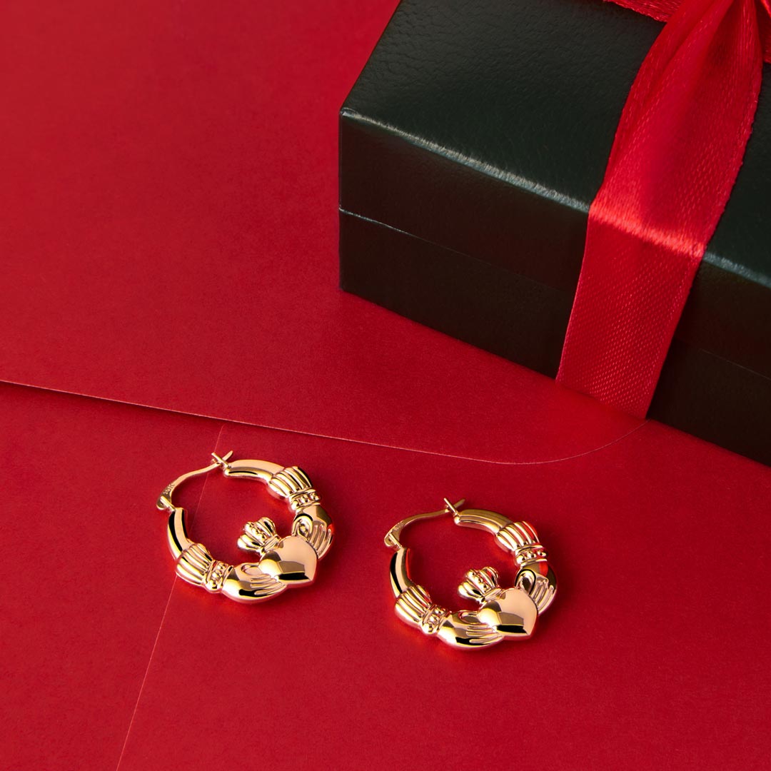 lifestyle image of Claddagh Hoop earrings in yellow gold on the red background