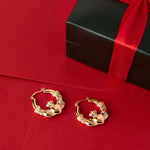 lifestyle image of Claddagh Hoop earrings in yellow gold on the red background