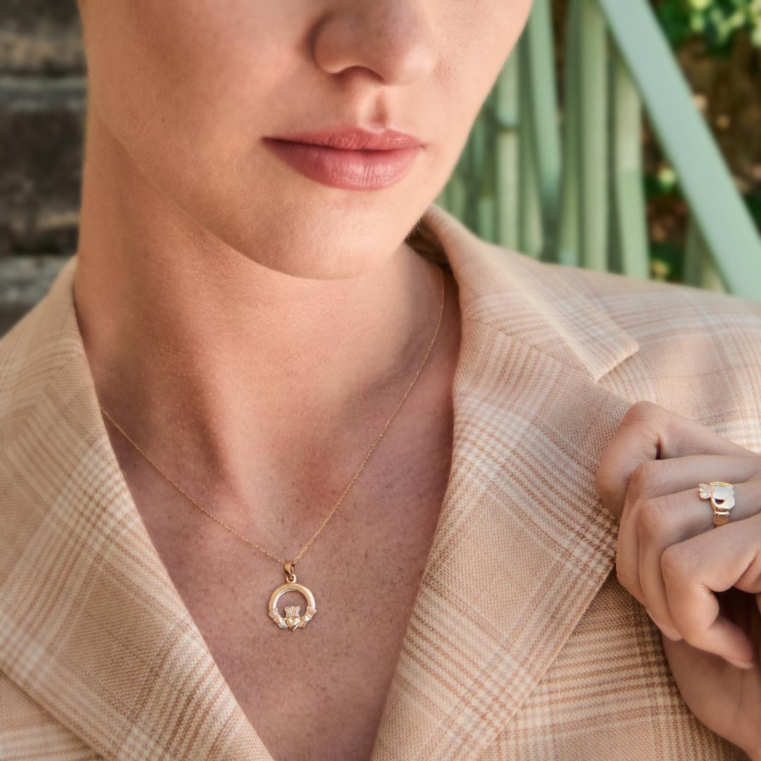 Close-up of a woman wearing a gold Claddagh pendant outdoors
