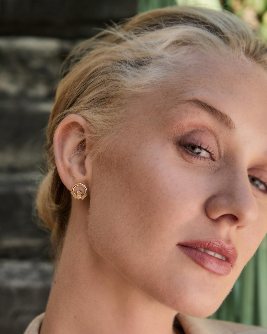 Close-up of a woman wearing gold Claddagh earrings with a blurred background