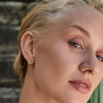 Close-up of a woman wearing gold Claddagh earrings with a blurred background