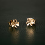 gold shamrock stud earrings on dark green background