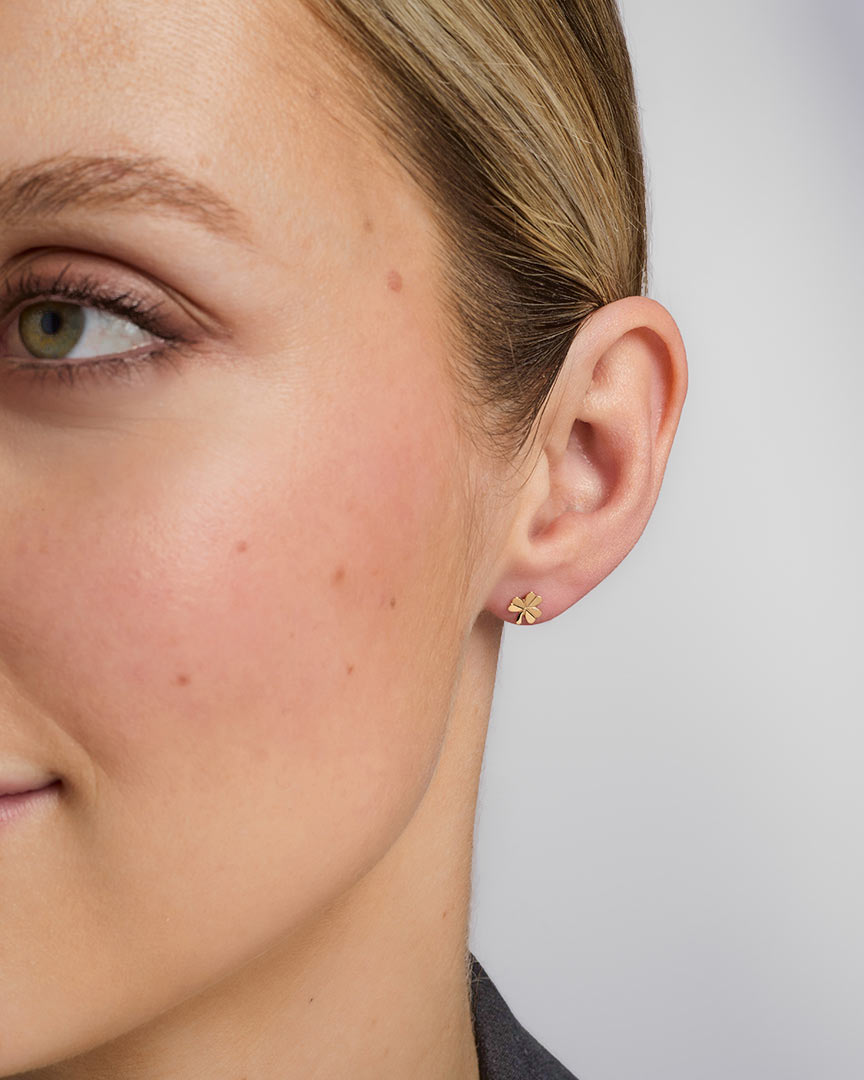 close-up image of gold shamrock stud earrings on a model