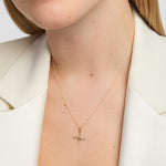 A close-up of a model wearing a delicate gold st Brigid's cross pendant necklace, styled with a white blazer