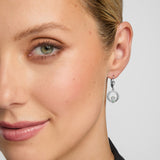 close-up image of female model wearing green crystal centre Claddagh drop earrings against grey background