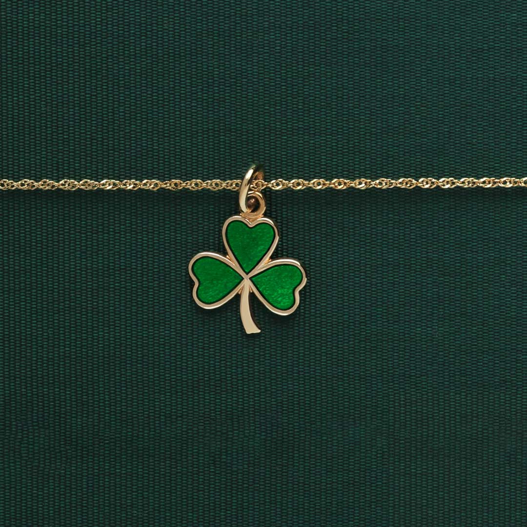 lifestyle image of  Solvar green enamelled gold shamrock necklace on green background