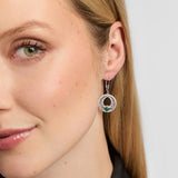 A close-up of a woman's ear and side profile wearing a silver Celtic Claddagh Drop earrings with a circular halo design and a green teardrop-shaped stone at the centre.