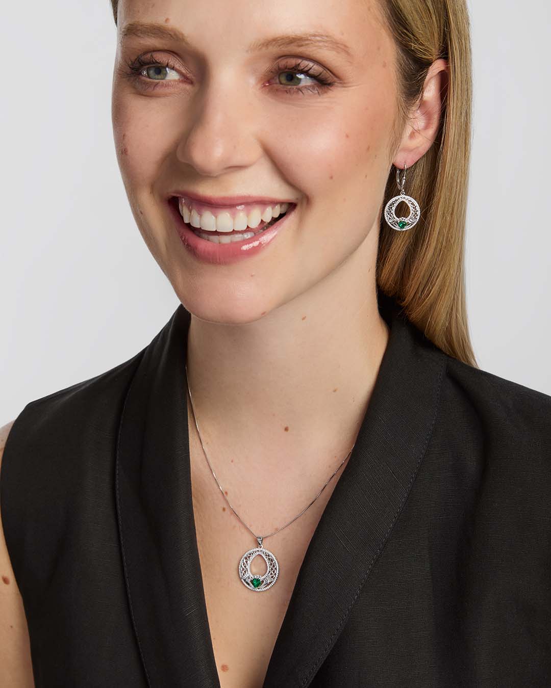 a female model wearing matching celtic Claddagh necklace and earrings with a green cubic zirconia Claddagh heart
