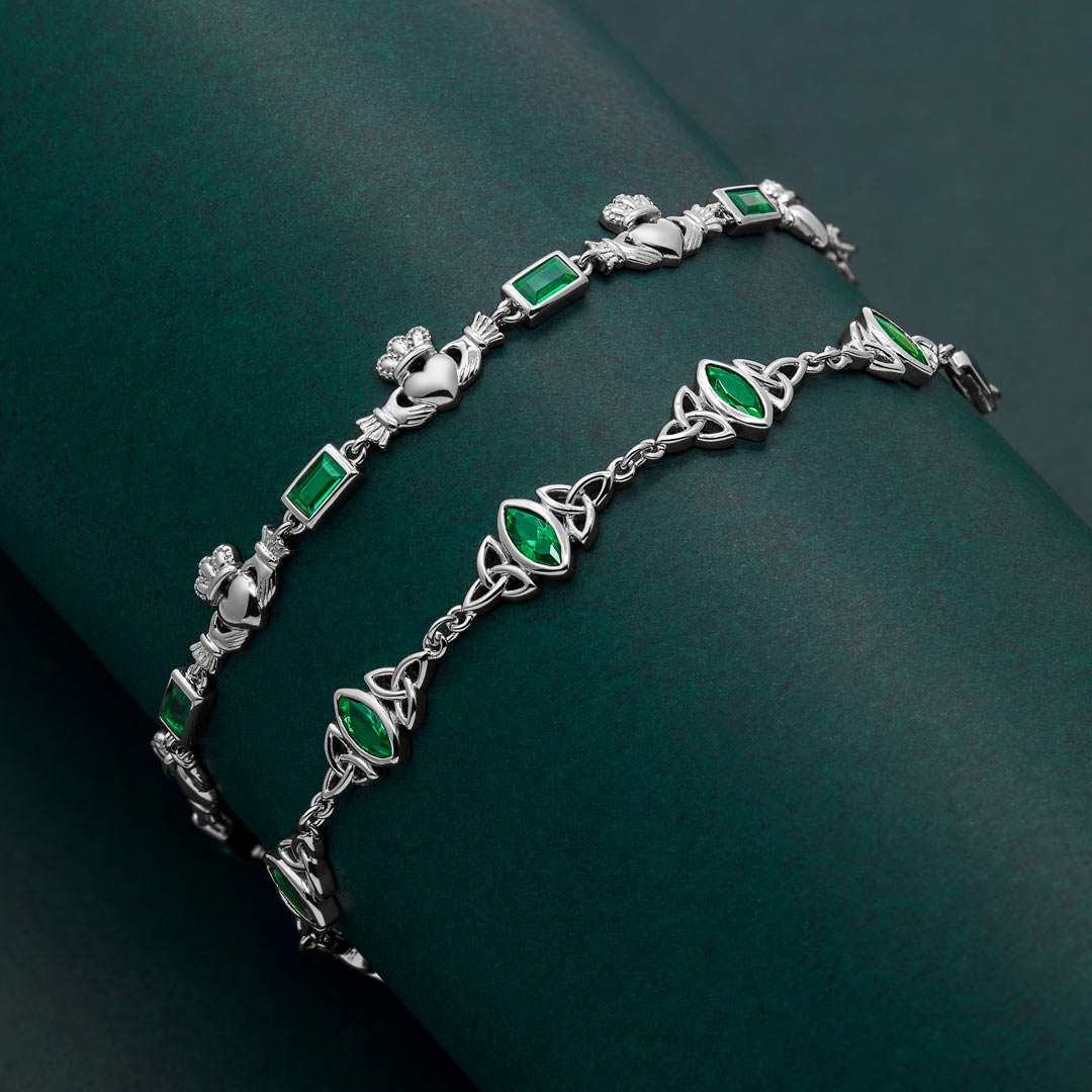 lifestyle shot of silver claddagh and trinity knot bracelets with green gemstones on a dark green background