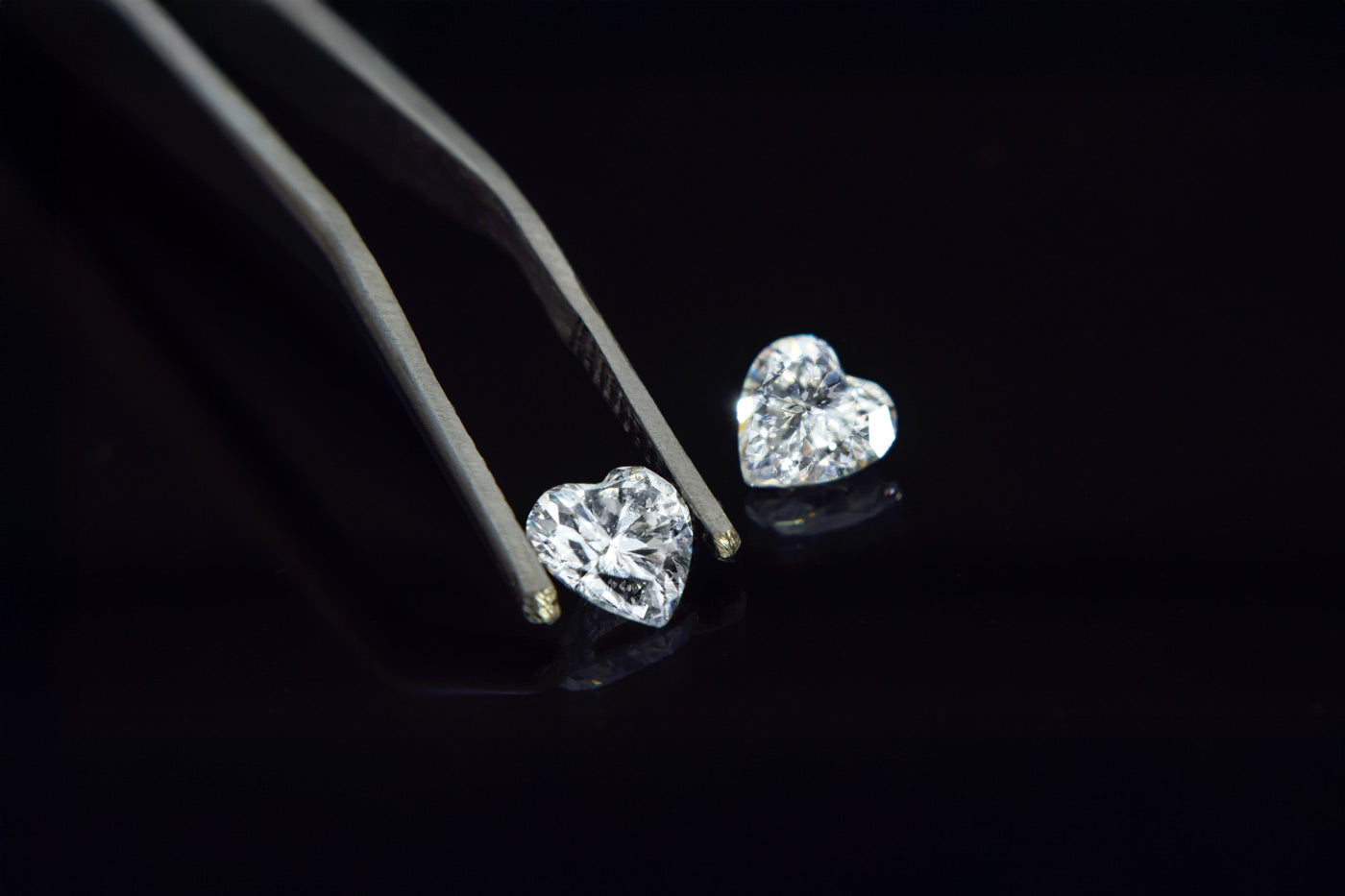 Heart-shaped diamond held in tweezers on a black background