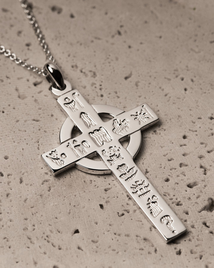 Silver cross pendant with engraved designs on a textured surface
