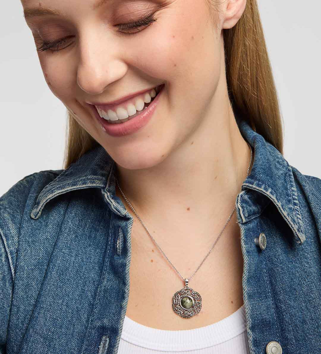 A close-up of a smiling woman wearing a Round Connemara marble and marcasite pendant with intricate interwoven Celtic knotwork design on a silver chain