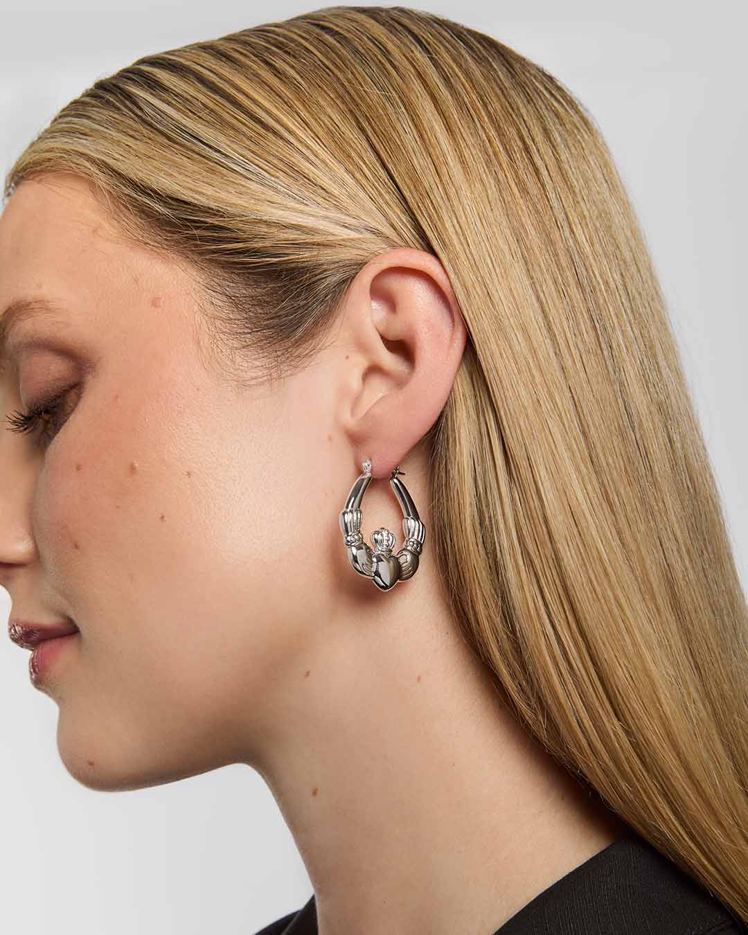 A model wearing large silver Claddagh hoop earrings, featuring the traditional Irish symbol of love, loyalty, and friendship