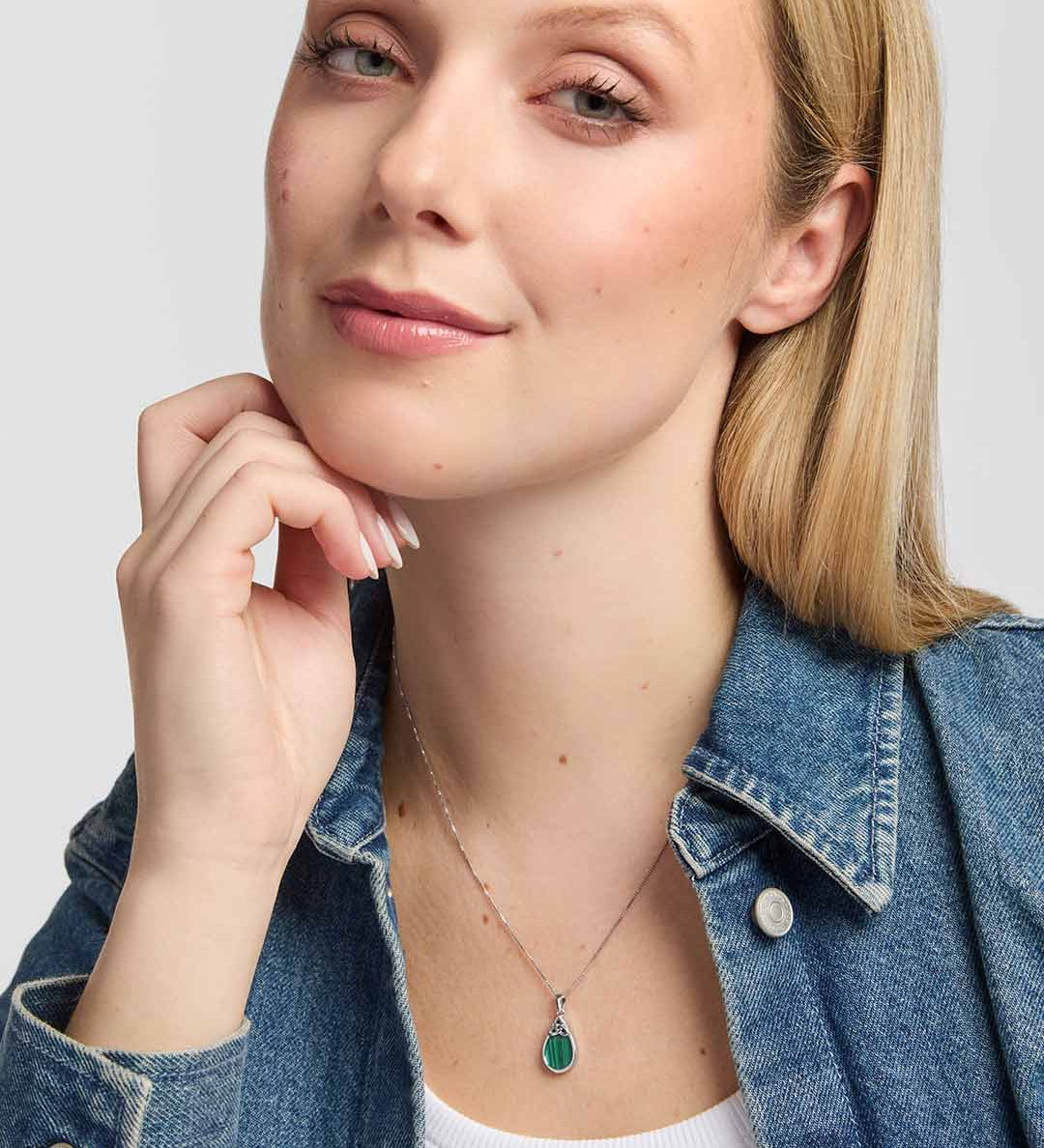 Model wearing an elegant teardrop pendant which showcases a rich green Malachite stone within a smooth polished silver frame, with an intricate Trinity Knot adding a distinctive Celtic finish.