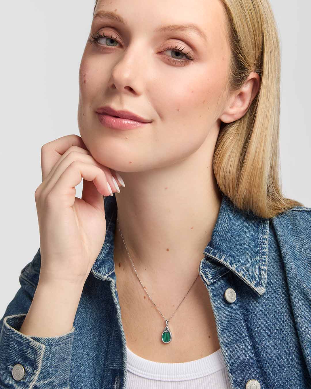 Model wearing an elegant teardrop pendant which showcases a rich green Malachite stone within a smooth polished silver frame, with an intricate Trinity Knot adding a distinctive Celtic finish.