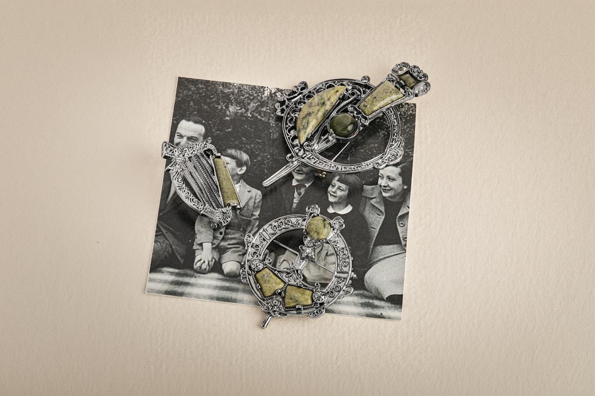 Three Celtic-style brooches with green marble stone inlays displayed on top of a vintage black-and-white photograph against a cream-colored background.