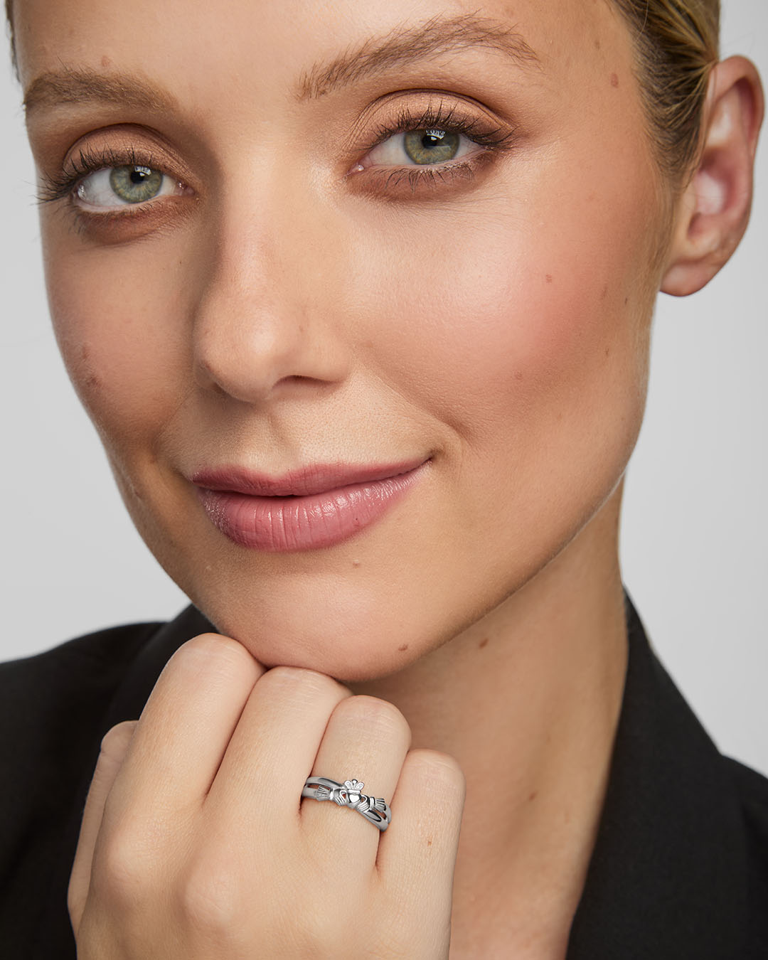 Close-up of a woman wearing a silver Claddagh ring on a plain background