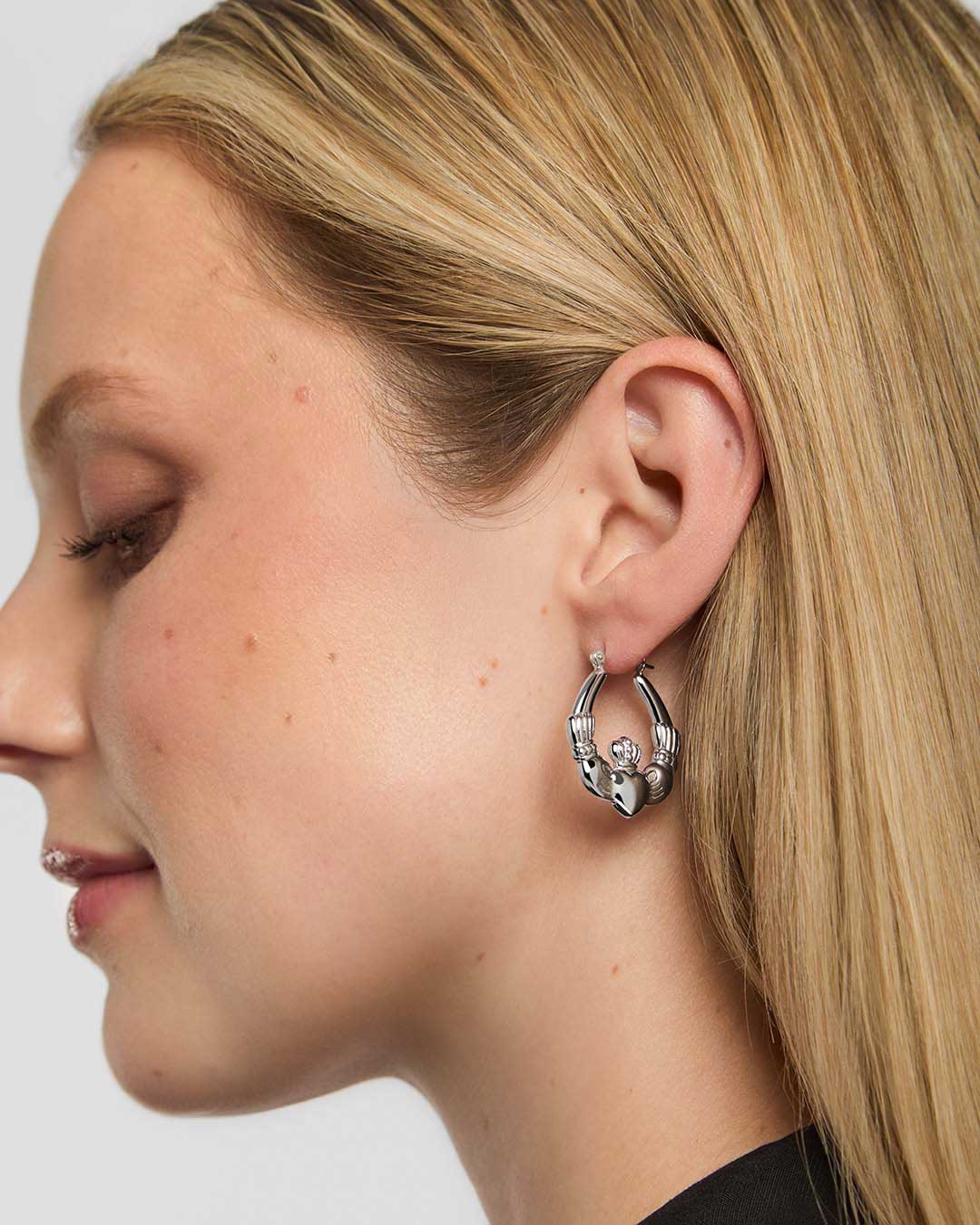 Close-up of a woman wearing a silver Claddagh hoop earring on a plain background