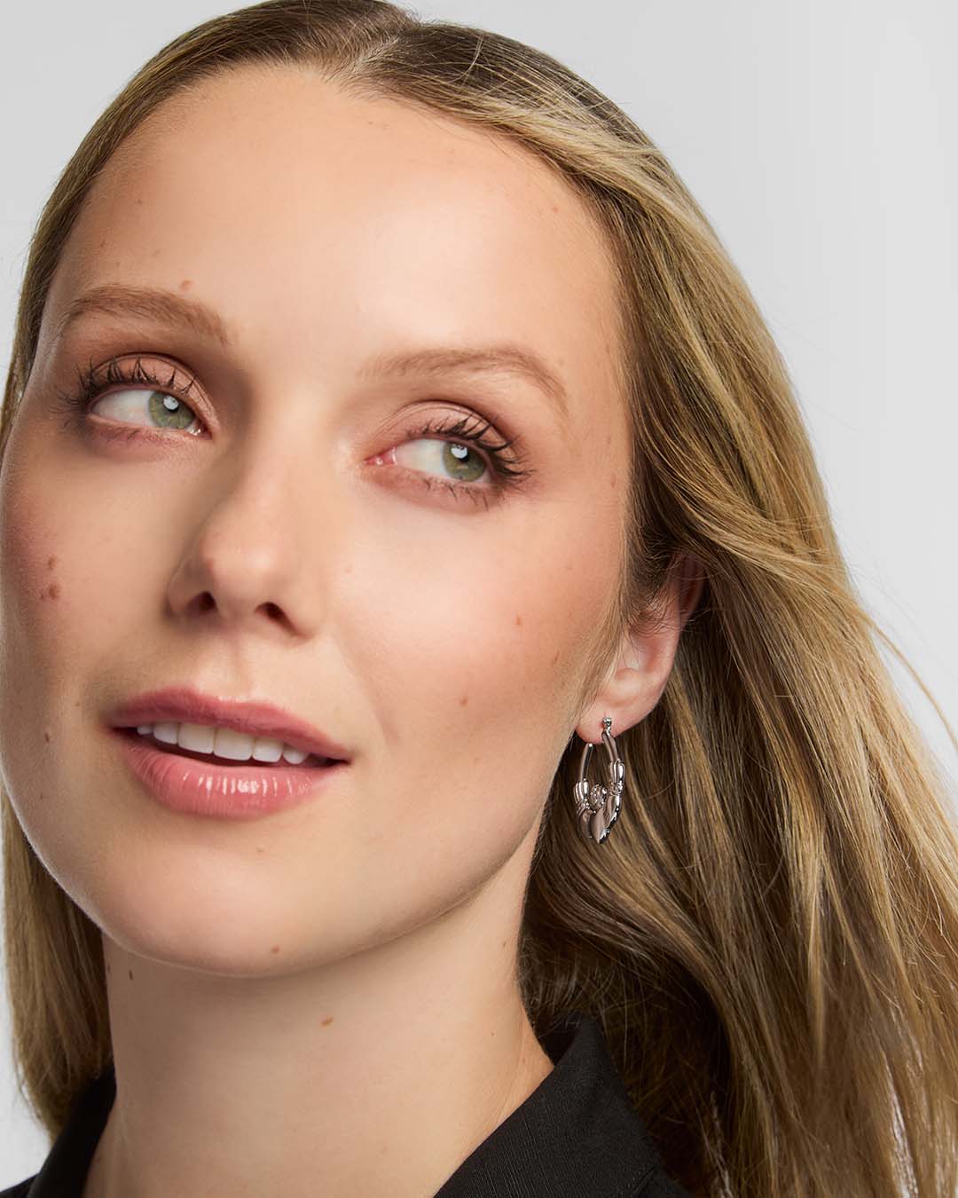 Close-up of a woman with blonde hair and Claddagh hoop earrings against a neutral background