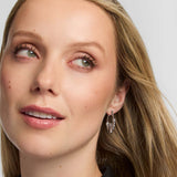 Close-up of a woman with blonde hair and Claddagh hoop earrings against a neutral background