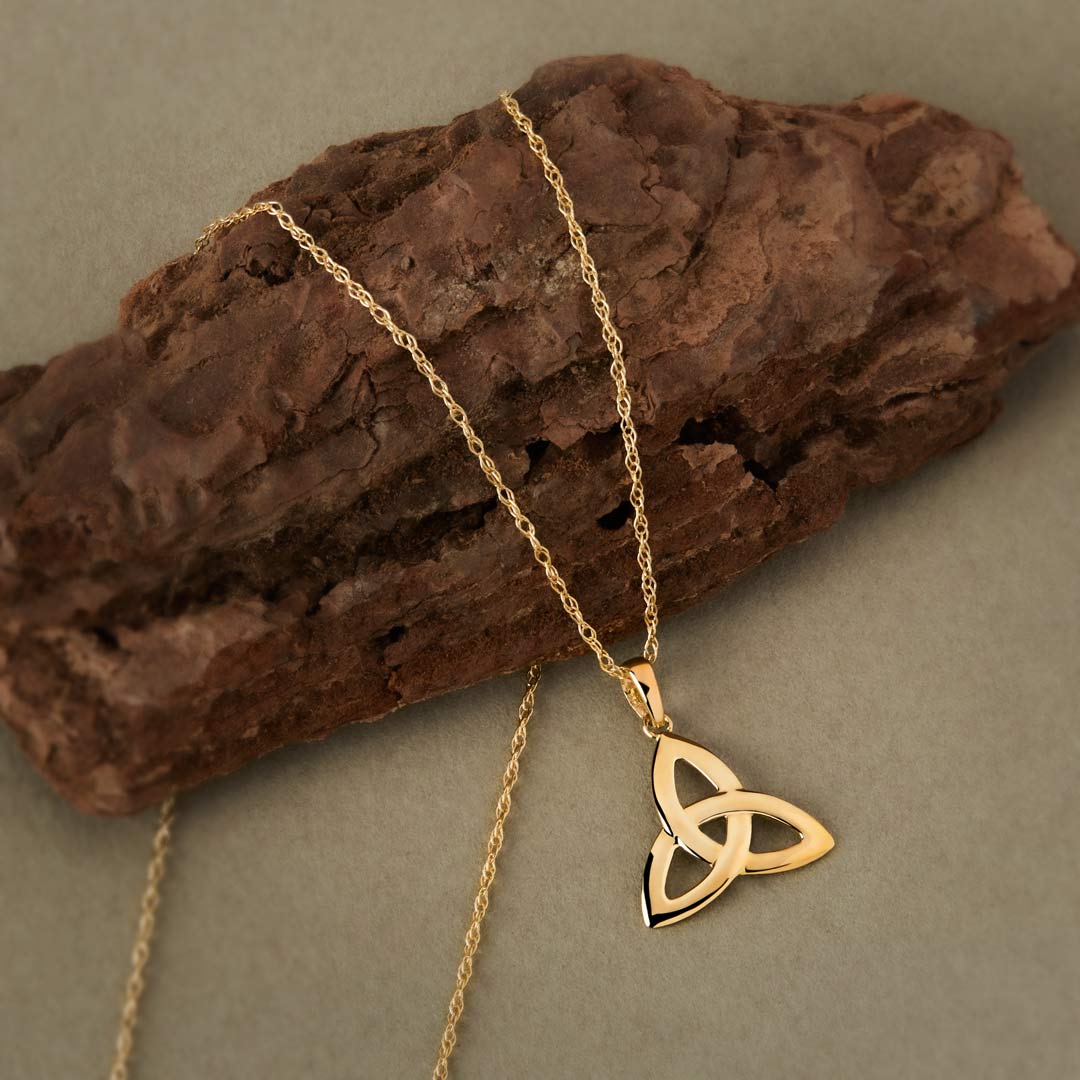 lifestyle image of yellow gold Celtic Trinity knot pendant on a textured surface