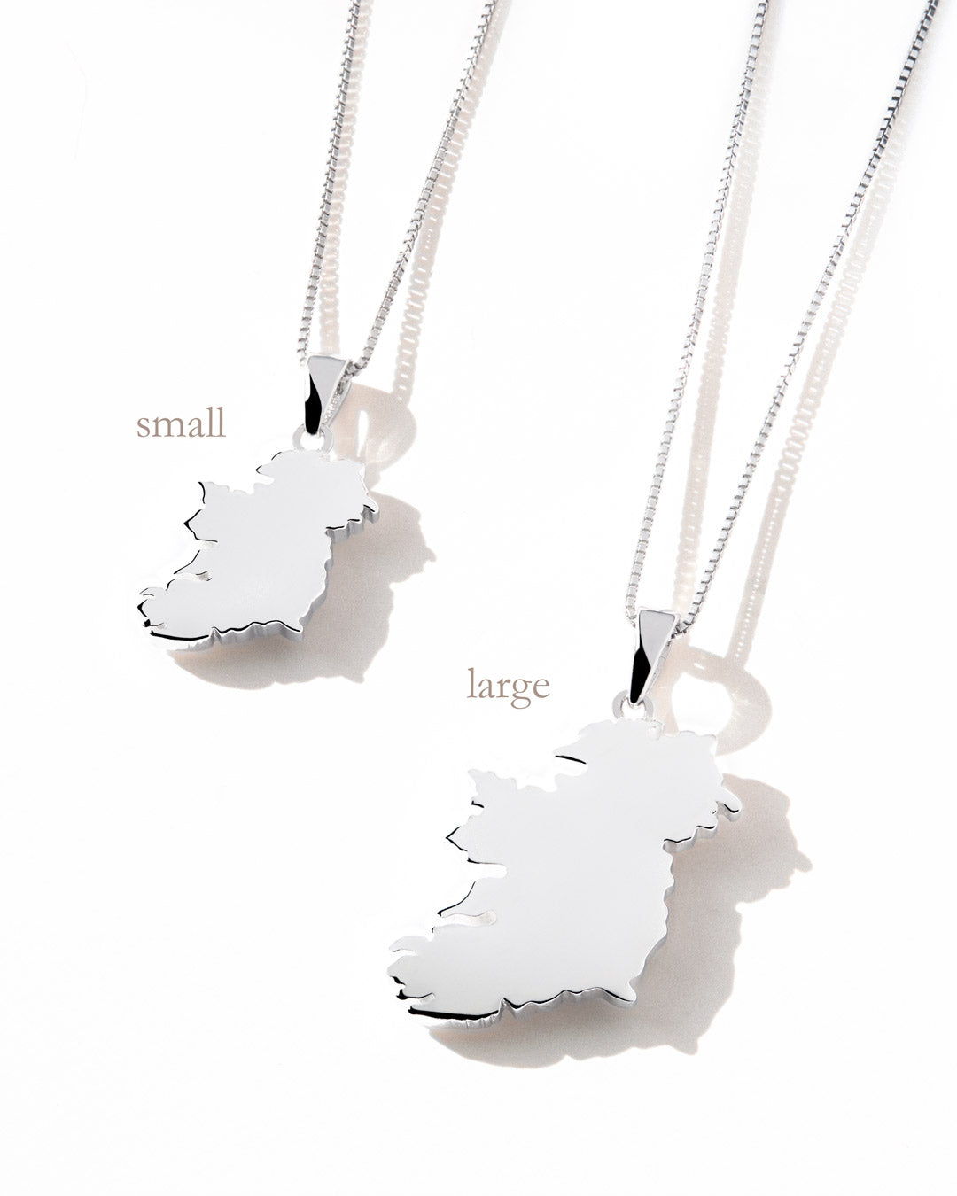 Two silver Ireland map pendant necklaces in small and large sizes, displayed side-by-side on a white surface with soft shadows