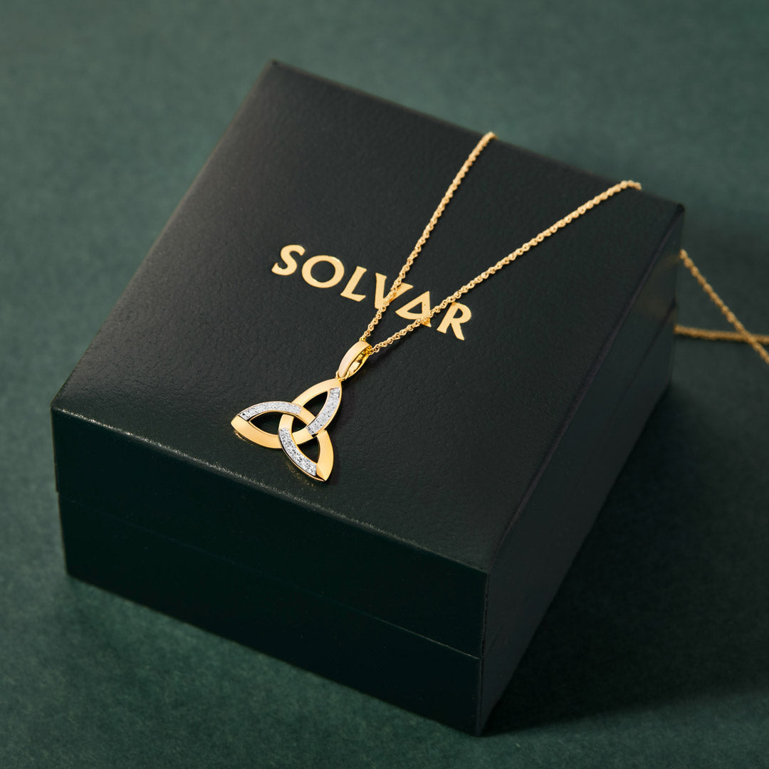 Gold necklace with a Trinity knot design on a Solvar jewellery box against a green background